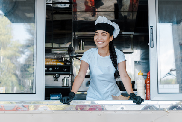feliz asiático mulher no chapéu e chef uniforme sorrindo em comida caminhão
  - Foto, Imagem