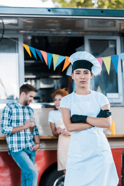 selectieve focus van Aziatische chef-kok staande met gekruiste armen in de buurt van Food truck en klanten  - Foto, afbeelding