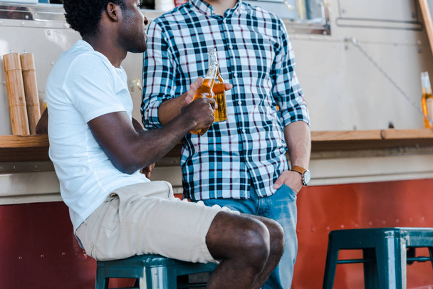 vista ritagliata di uomini multiculturali clinking bottiglie con birra vicino camion cibo
  - Foto, immagini