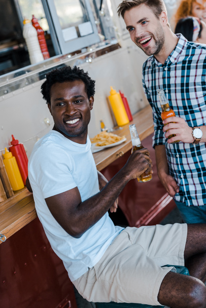 επιλεκτική εστίαση των χαρούμενοι πολυπολιτισμικοί άνδρες που κρατούν μπουκάλια με μπίρα  - Φωτογραφία, εικόνα