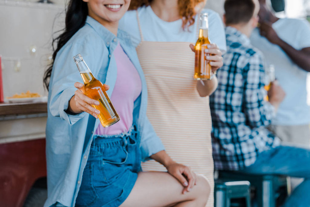 cropped view of happy girls holding bottles of beer near food truck - Foto, Imagem