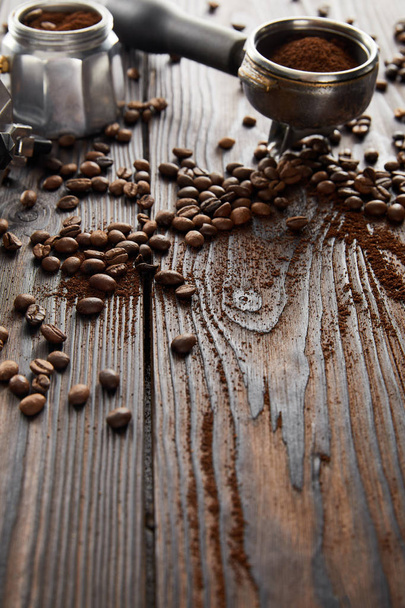 Portafilter in de buurt van geiser koffiezetapparaat op donker houten oppervlak met koffiebonen - Foto, afbeelding