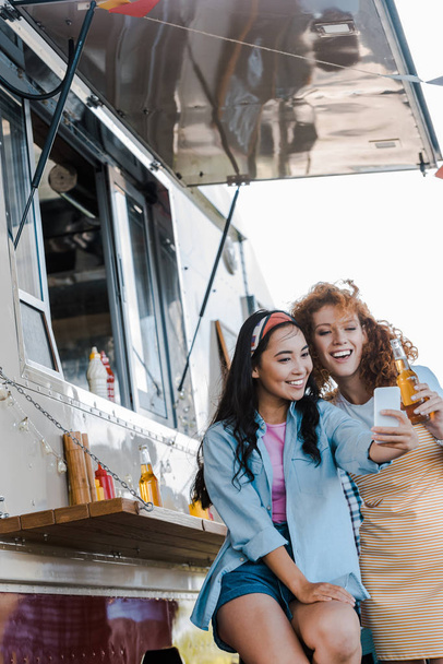 foco seletivo de meninas multiculturais alegres tomando selfie perto de caminhão de alimentos
 - Foto, Imagem