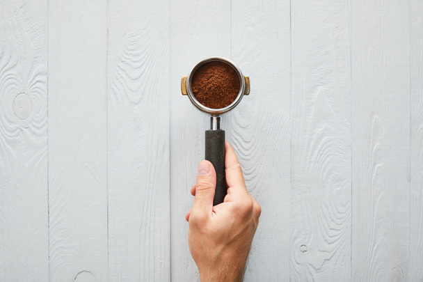 Top View van man Holding filterhouder met koffie op wit houten oppervlak - Foto, afbeelding