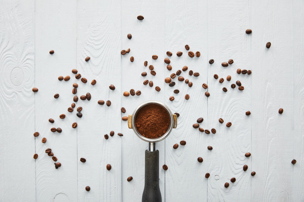 Top view of portafilter with coffee on white wooden surface with scattered coffee beans - Photo, Image