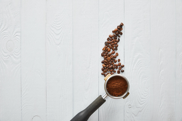 Вид сверху портафильтра с кофе на белой деревянной поверхности с кофейными бобами
 - Фото, изображение