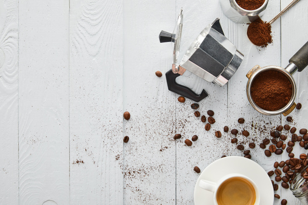 Top view of geyser coffee maker near portafilter, spoon and cup of coffee on white wooden surface with coffee beans - Photo, Image