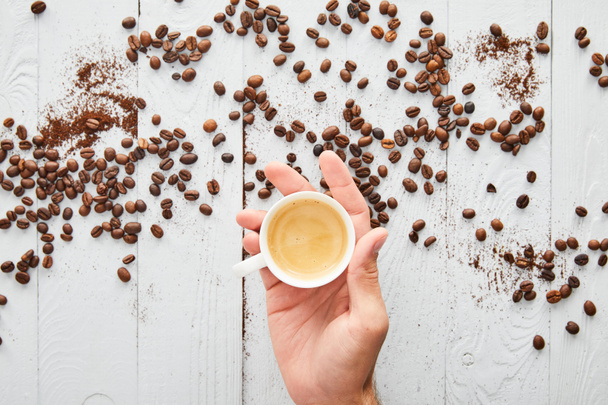 Felülnézet az ember kezében csésze kávét karja alatt fehér fa felülete kávébab - Fotó, kép