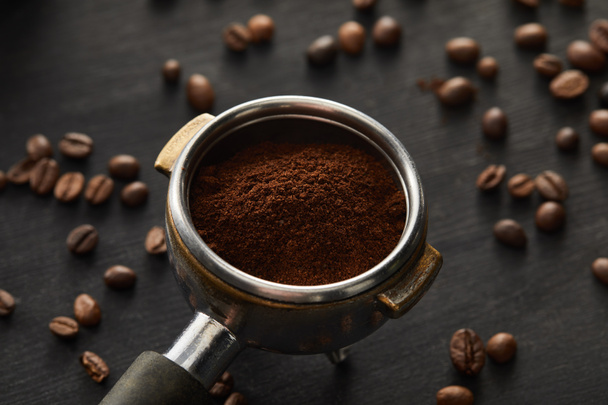 Portafilter filled with fresh coffee on dark wooden surface with coffee beans - Photo, Image