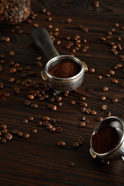 Portafilters with ground coffee on dark wooden surface with coffee beans - Фото, зображення