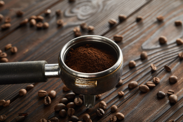 Portafilter täynnä tuoretta jauhettua kahvia tummalla puupinnalla kahvipapuja
 - Valokuva, kuva