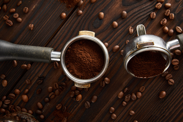 Portafilters with ground coffee on dark brown wooden surface with coffee grains - Φωτογραφία, εικόνα