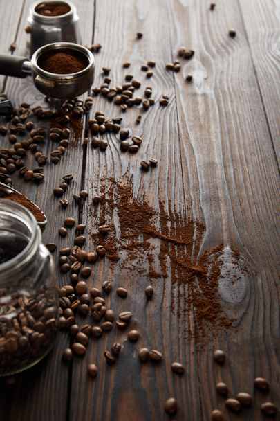 Tarro de vidrio cerca de portafilter y parte de la cafetera géiser en la superficie de madera oscura con granos de café
 - Foto, Imagen
