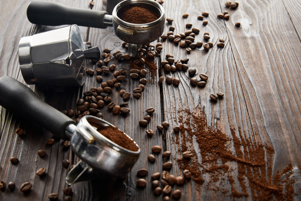 Cafetera géiser entre portafilters en superficie de madera marrón oscuro con granos de café
 - Foto, Imagen