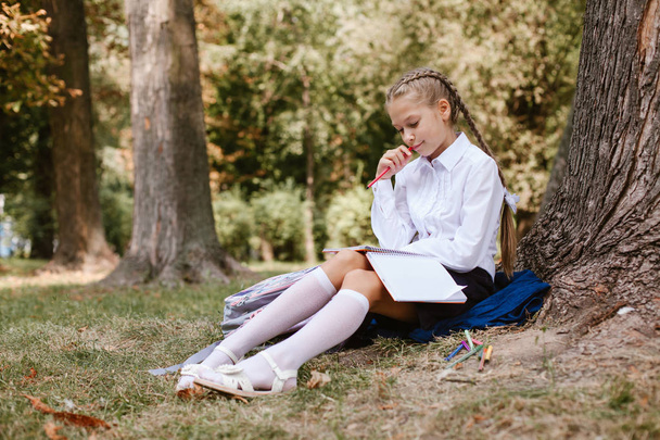 Koulutyttö opettaa puistossa puun alla. Koulutyttö istuu puiston puun alla.
 - Valokuva, kuva