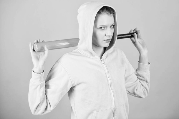 Woman play baseball game or going to beat someone. Woman in baseball sport. Baseball female player concept. She is dangerous. Girl hooded jacket hold baseball bat blue background. Brutal and bully - Foto, afbeelding