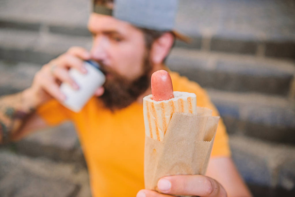 Hot dog sausage in bun. Bearded man eating unhealthy hot dog sandwich. Hipster drinking coffee with hot dog during rest break. Caucasian guy enjoying hot dog traditional street cuisine - Foto, Bild