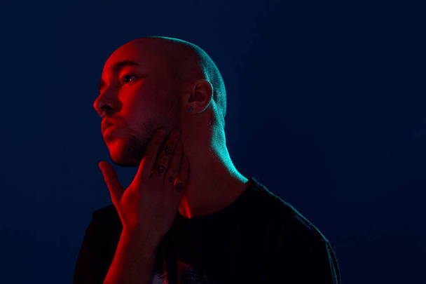 Studio shot of a young tattoed bald man posing against a blue background. 90s style. - Foto, Bild