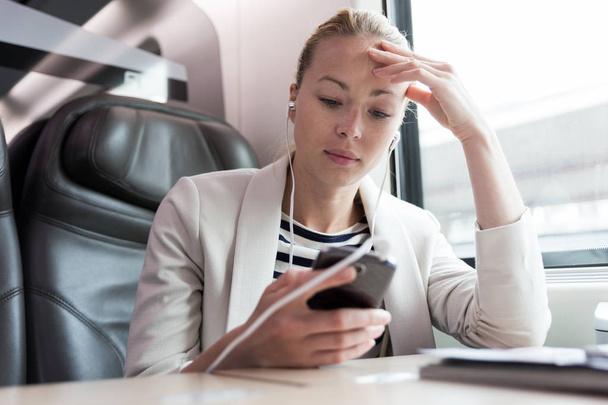 Bizneswoman komunikujących się przez telefon komórkowy podczas podróży pociągiem. - Zdjęcie, obraz