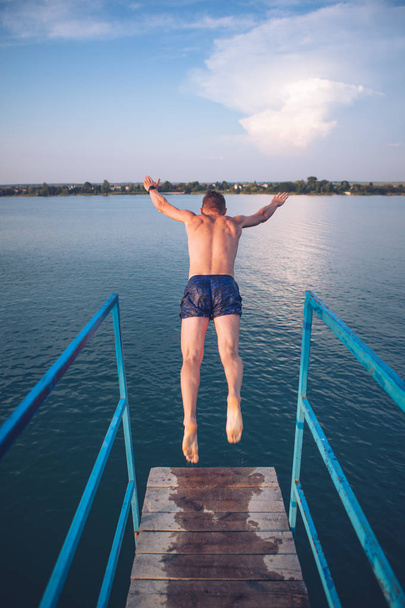 чоловік стрибає з вежі на озері вода на заході сонця
 - Фото, зображення
