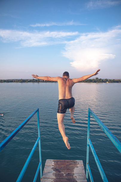 hombre saltando desde la torre en el agua del lago al atardecer
 - Foto, imagen