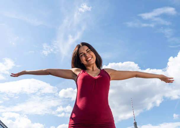 Szczęśliwy uśmiechnięta brunetka dziewczyna pozowanie z wyciągniętymi ramionami przeciwko błękitne niebo - Zdjęcie, obraz