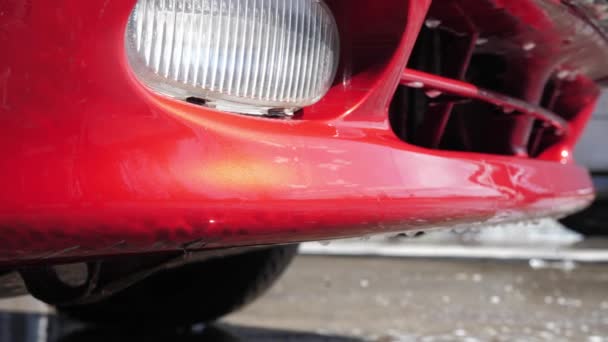 Water en geschuimd reinigingsmiddel afvoeren van een rode gewassen auto in een self-service auto wassen. 4k-beeldmateriaal. - Video