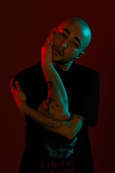 Studio shot of a young tattoed bald man posing against a red background. 90s style. - Photo, Image