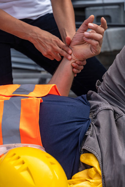 Immagine ritagliata delle mani di un paramedico che controlla la frequenza cardiaca di un operaio disteso infortunato sul lavoro
 - Foto, immagini