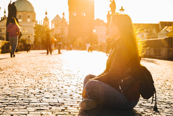 woman sitting on the ground at sunrise at charles bridge in Prague - Foto, imagen