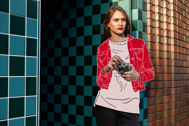 Csinos, fiatal modell, egy retro film kamera visel rajzfilm piros kabátot és fehér póló pózol az utcán. - Fotó, kép