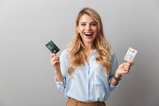 Pretty blonde business woman posing isolated grey wall background holding two credit cards. - Fotografie, Obrázek