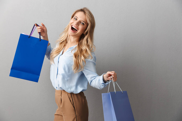 Happy excited young pretty blonde business woman posing isolated grey wall background holding shopping bags. - Foto, Imagem
