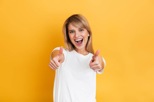 Happy young pretty blonde woman posing isolated over yellow wall background dressed in white casual t-shirt. - 写真・画像