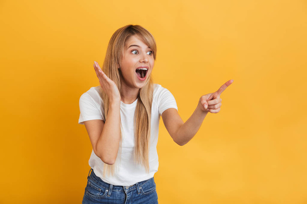 Happy young excited blonde woman posing isolated over yellow wall background pointing. - Valokuva, kuva