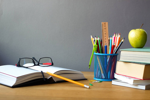 Back to school concept, school supplies, stack of books, green apple and open book with glasses on a wooden surface, selective focus - Photo, Image