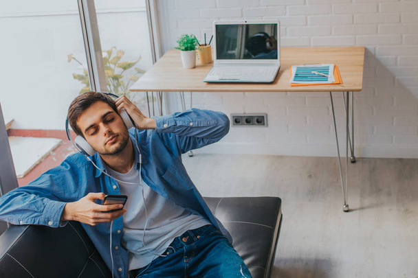 young man in the apartment with phone and headphones - Photo, Image