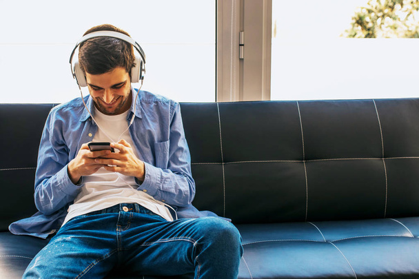 young man or teenager with mobile phone and headphones at home - Photo, Image