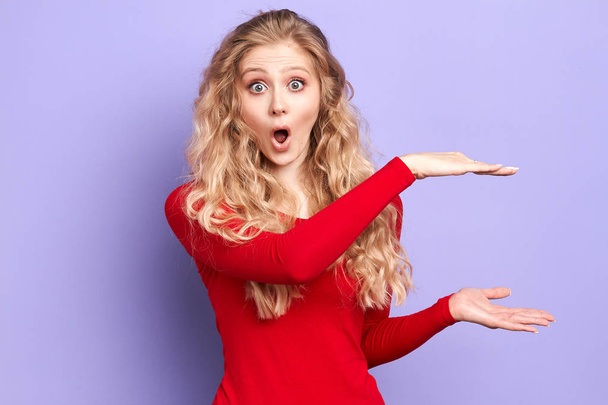 blonde emotional surprised young woman shows big size measure with palms - Foto, imagen