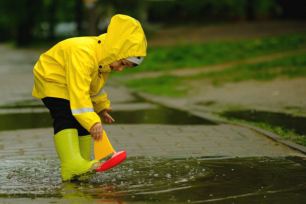 Счастливый ребенок играет в луже в летний дождливый день. мальчик в жёлтом плаще гуляет по парку
. - Фото, изображение