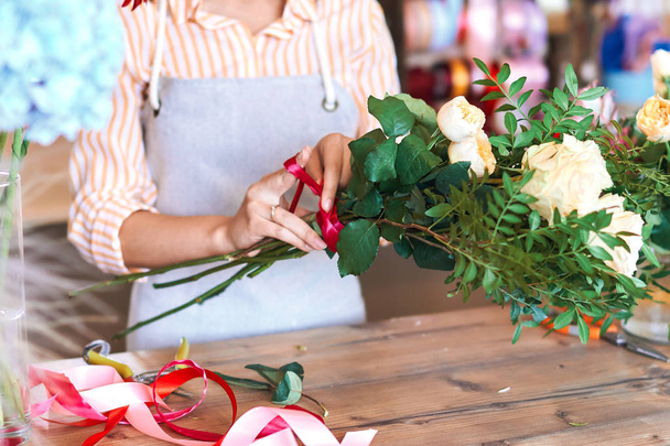 Owner of florist shop tying red ribbon around bunch of fresh white roses - Foto, afbeelding