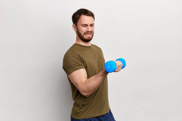 crying man raises a dumbbell with one hand with frowning face - Фото, изображение