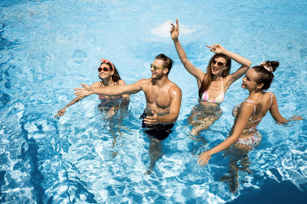 Company of young merry girls and guy are having fun in the swimming pool on the open air on a sunny summer day - Foto, Imagem