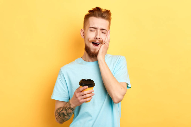 Sleepy man with closed eyes holding a disposable plastic cup and yawning - Foto, immagini