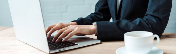 panoramic shot of businesswoman typing on laptop near cup of coffee  - Fotoğraf, Görsel