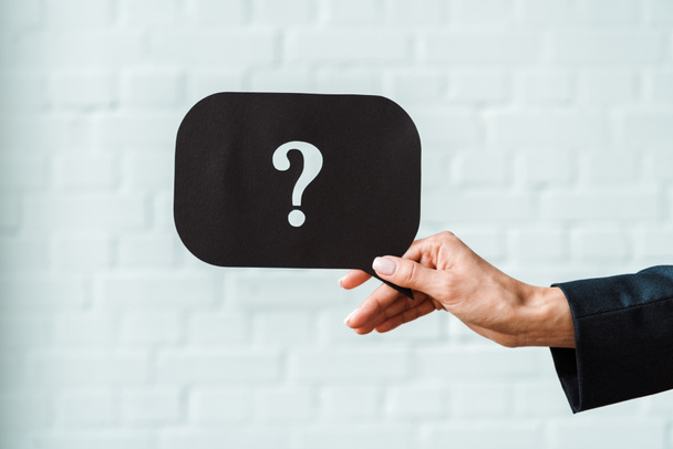 cropped view of woman holding black speech bubble with question mark near white brick wall  - Fotoğraf, Görsel