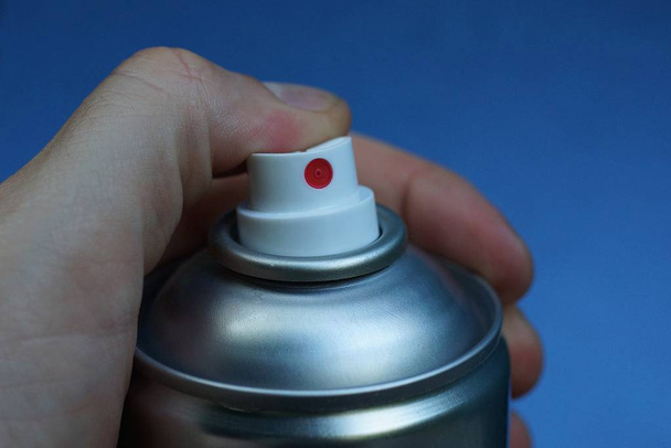 палец нажимает белый пластиковый диспенсер на сером металлическом баллончике на голубом фоне
 - Фото, изображение