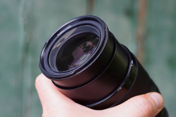 una lente de cámara abierta negra en una mano sobre un fondo verde
 - Foto, Imagen