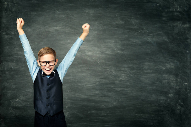 Criança da escola feliz levantou os braços, garoto inteligente sobre quadro negro
 - Foto, Imagem