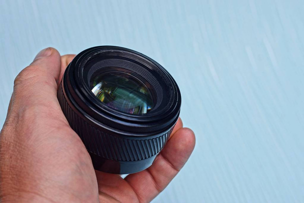 ένα μαύρο ανοιχτό φακό κάμερας σε ένα χέρι σε μπλε φόντο - Φωτογραφία, εικόνα